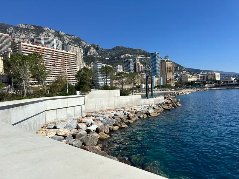 View across Larvotto beach and Monaco's eastern coastline from the new Mareterra district, with the Mediterranean in the foreground and Monte-Carlo skyline beyond