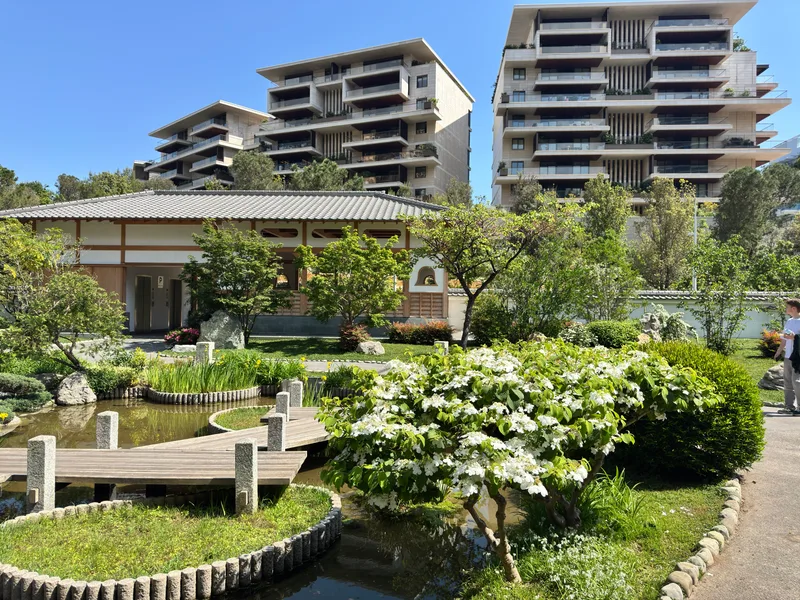 Monaco's Japanese Garden with Jardin d'Eau residential complex beyond, showing the garden's sculpted landscaping and still water features at the Larvotto boundary