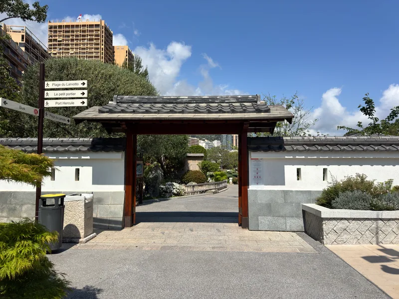 The entrance to Monaco's Japanese Garden at the junction of Larvotto and Mareterra, with manicured hedging and stone gateway framing the garden beyond